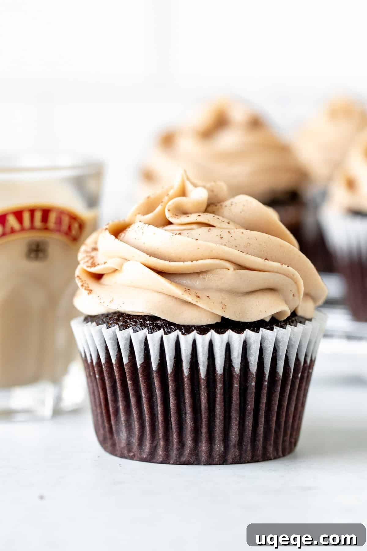 Irish Cream Dream Cupcakes 2 A perfectly frosted Baileys cupcake next to a small glass of Baileys Irish Cream, inviting indulgence.