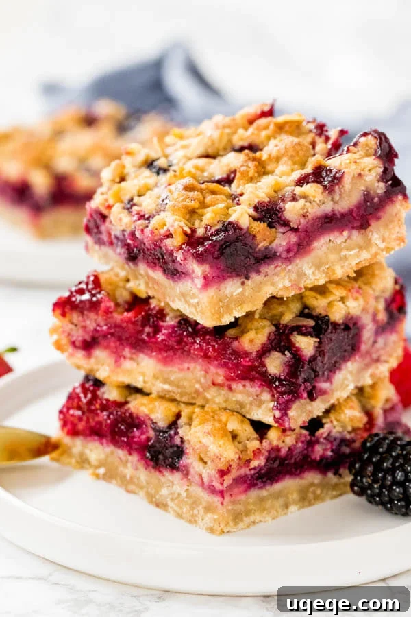 Berry Burst Crumble Squares 2 Three stacked mixed berry oatmeal crumble bars on a white plate, showcasing the buttery oatmeal and vibrant berry layers.