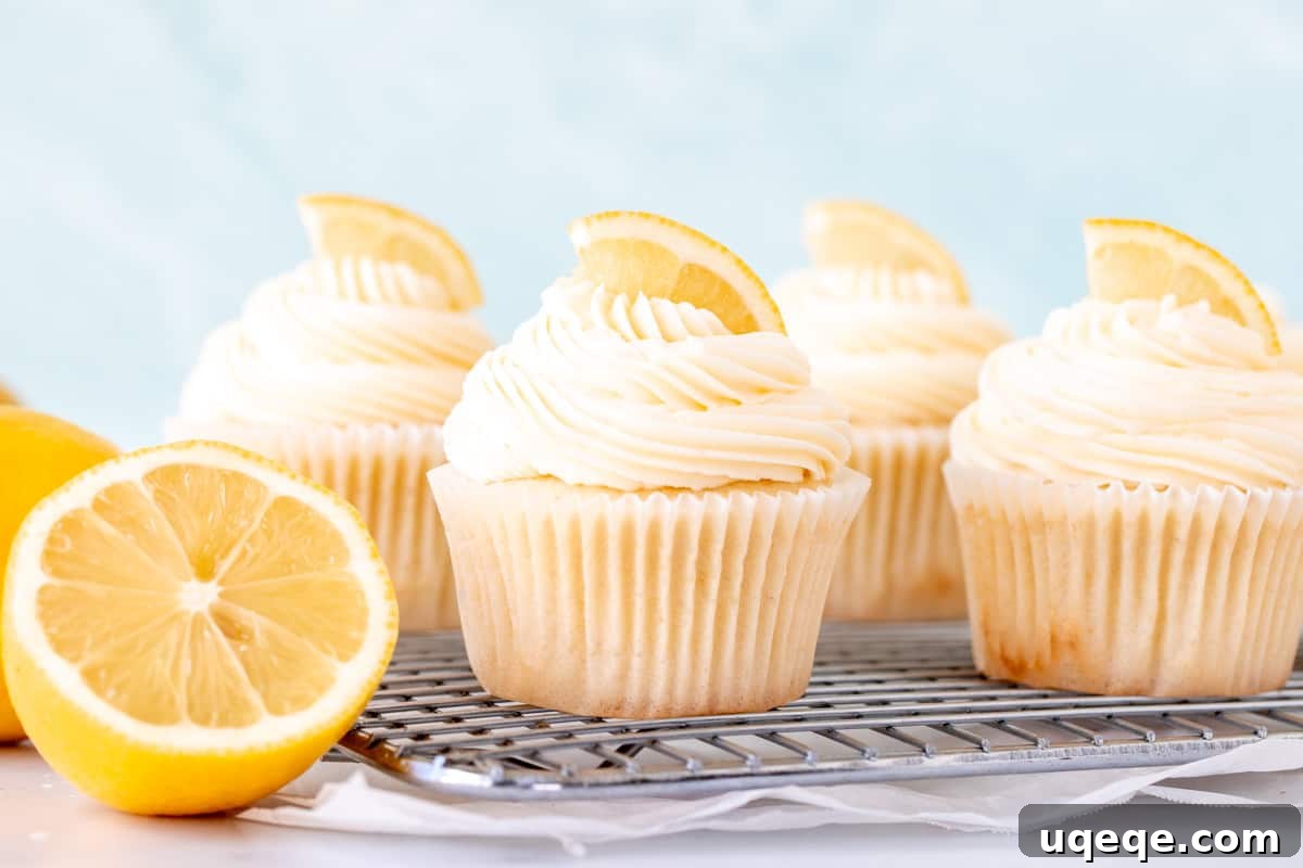 Moist lemon cupcakes topped with tangy lemon frosting, cooling on a wire rack next to a freshly cut lemon half, ready to be enjoyed.