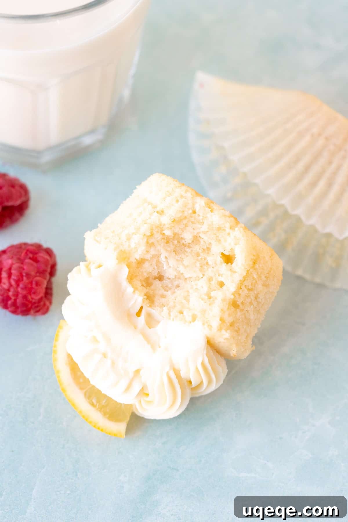 A lemon cupcake with a bite taken out, resting on its side, revealing its moist crumb and creamy lemon frosting.