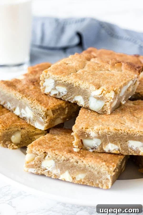 Decadent White Chocolate Macadamia Blondies 3 A plate of fudgy white chocolate macadamia nut blondies with a glass of milk in the background.
