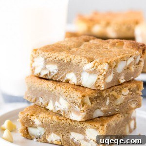 A stack of 3 white chocolate macadamia nut blondies with a glass of milk in the background.