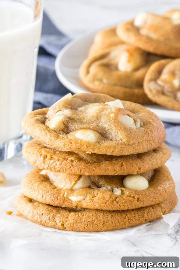 Decadent White Chocolate Macadamia Cookies 2 A stack of soft, chewy white chocolate macadamia cookies with golden edges. With a glass of milk and extra plate of cookies in the background.