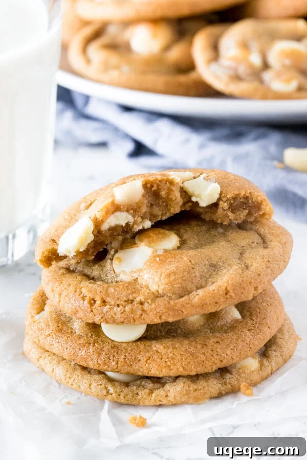 Decadent White Chocolate Macadamia Cookies 5 A stack of subway copycat white chocolate macadamia cookies with the top cookie broken in half to show the chewy center.