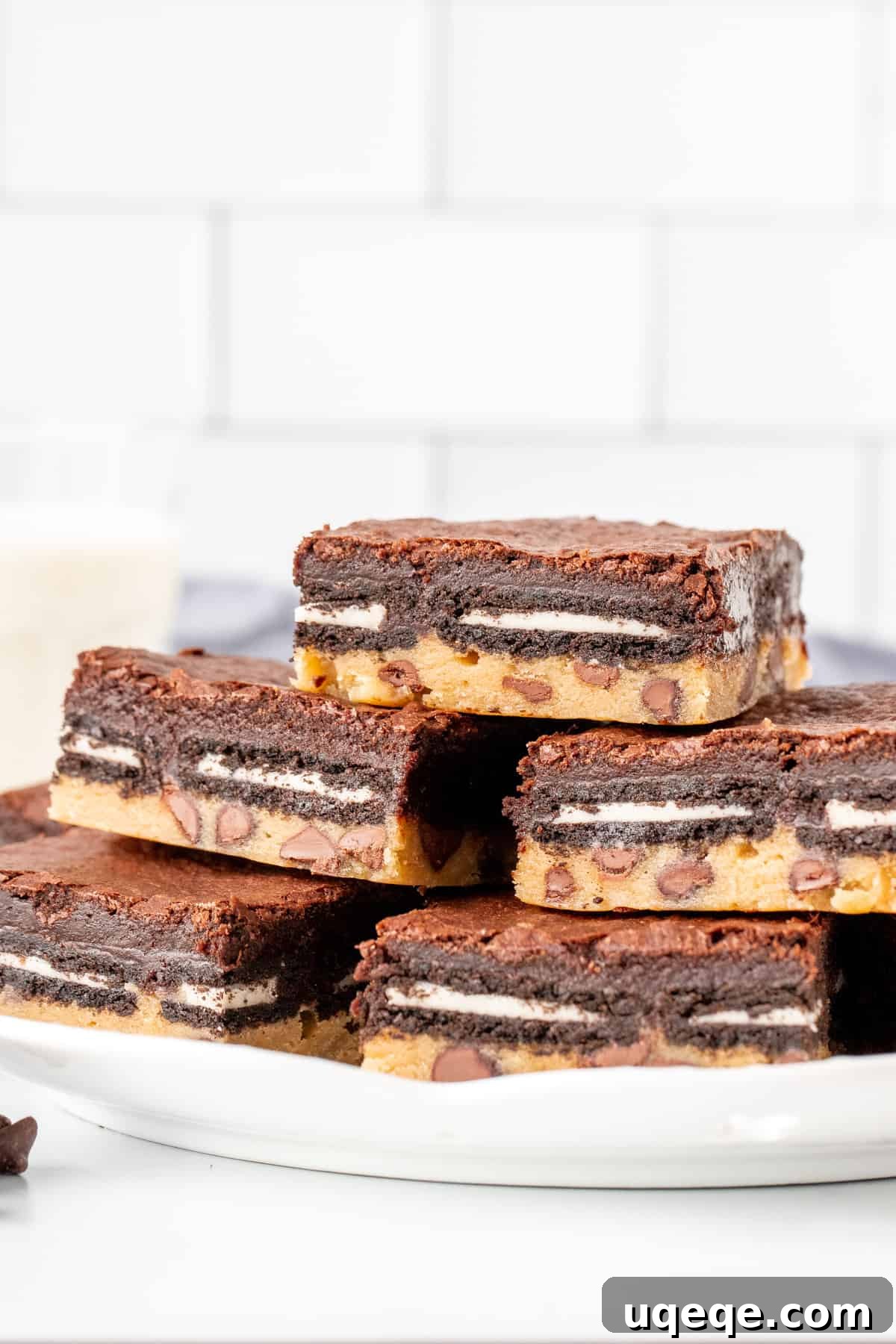 Slutty Brownies: Perfectly Fudgy and Deliciously Homemade 3 A close-up view of a plate with two stacked layered brownies, showing the rich chocolate chip cookie base, the iconic Oreo layer, and the dark, fudgy brownie top. A bite has been taken out of the top brownie.