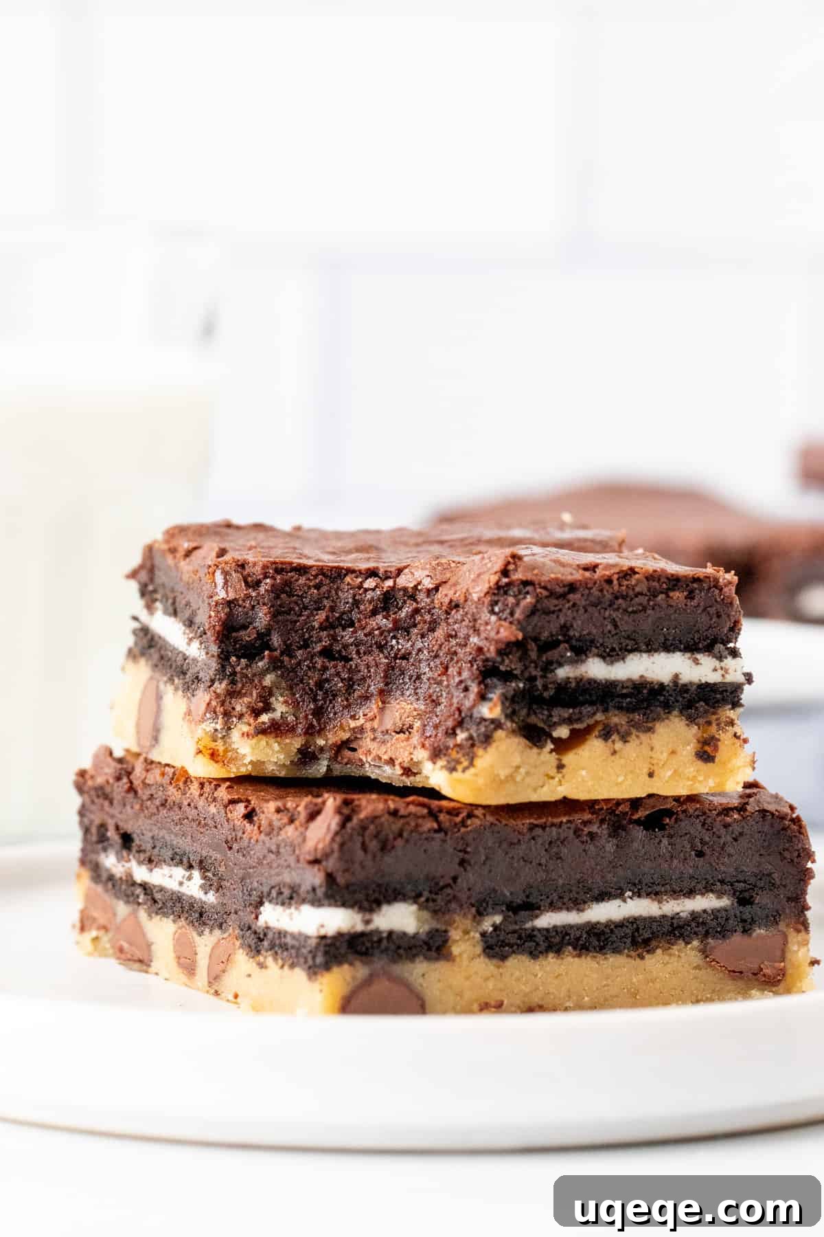 Slutty Brownies: Perfectly Fudgy and Deliciously Homemade 10 Two rich layered brownies, one stacked on top of the other, with a visible bite taken from the top brownie, revealing the distinct cookie, Oreo, and fudgy brownie layers.