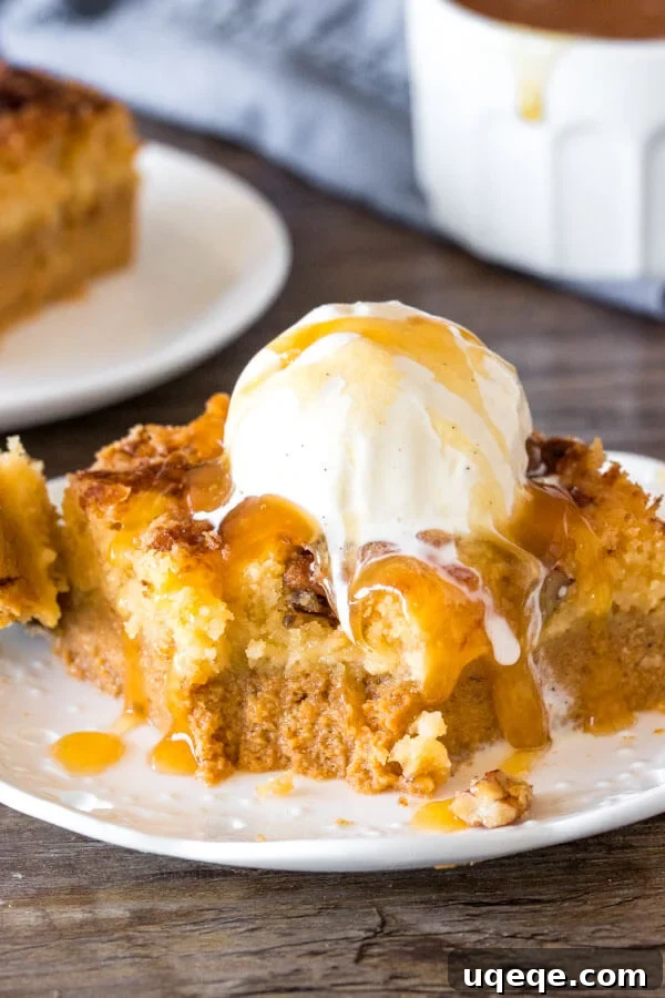 A perfectly sliced piece of pumpkin dump cake, revealing its creamy pumpkin base and gooey butter cake topping, served alongside a scoop of melting ice cream.