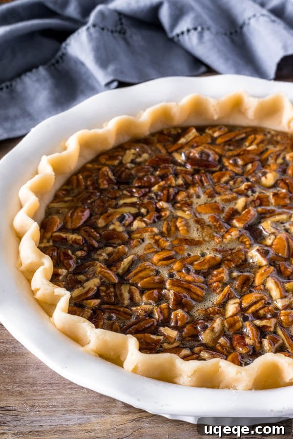 An unbaked pecan pie resting in a pie dish, showcasing the chopped pecans at the bottom and the rich, glossy filling poured over them, ready for the oven.