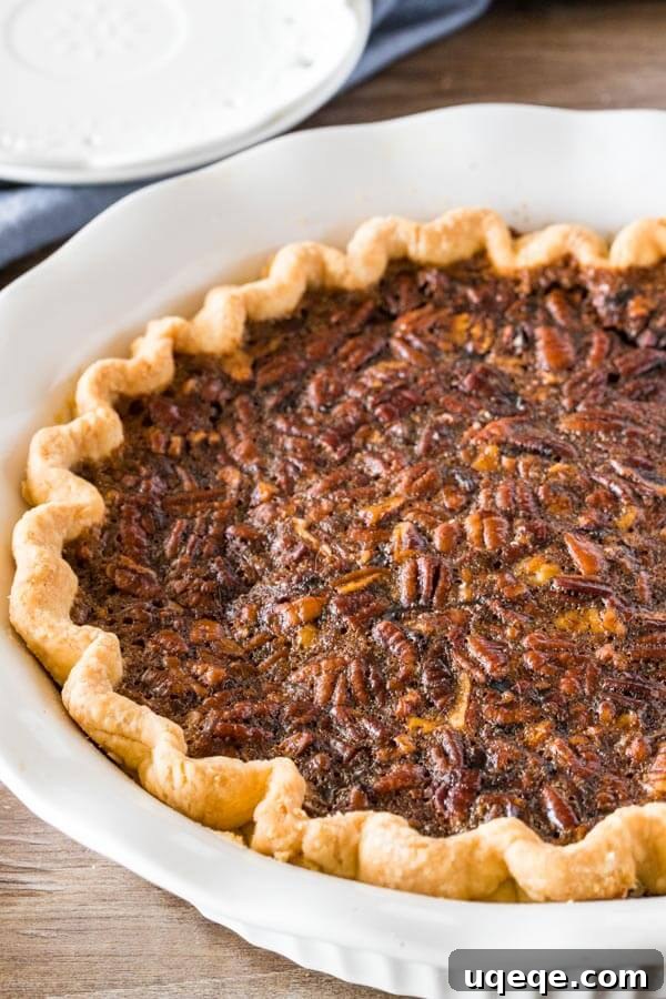 A freshly baked pecan pie gleaming in a white ceramic pie dish, with its golden-brown crust and glistening pecan topping, just removed from the oven.
