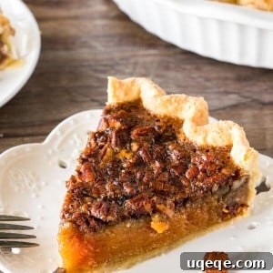 A slice of pecan pie with fluted edges on a white plate with the rest of the pie in the background.