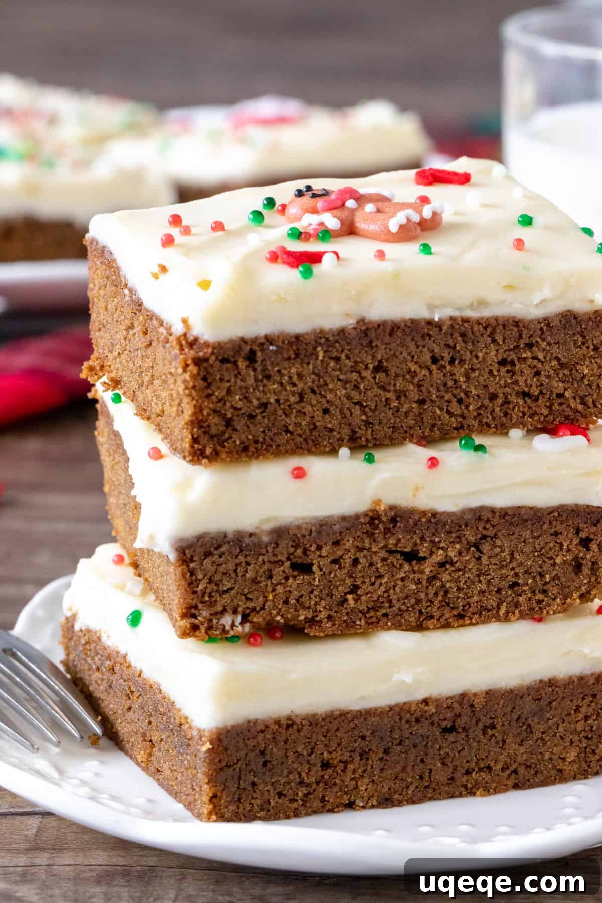 A delightful stack of three gingerbread cookie bars, richly topped with cream cheese frosting and festive sprinkles, perfect for holiday celebrations.