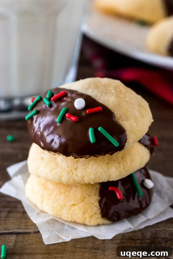 A stack of three buttery, melt-in-your-mouth chocolate-dipped shortbread cookies, perfectly presented with a refreshing glass of milk, ideal for Christmas or any festive occasion.