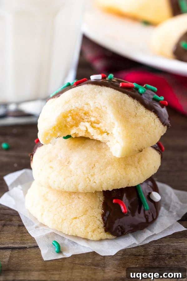 A stack of three beautifully prepared chocolate-dipped shortbread cookies, with a tempting bite taken out of the top cookie, revealing its tender, buttery interior and the perfectly set chocolate coating.