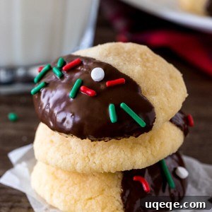 A charming close-up of a stack of three chocolate-dipped shortbread cookies alongside a refreshing glass of milk, perfectly conveying their delicious appeal.