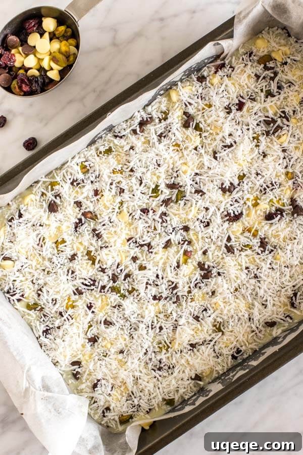 Christmas magic cookie bars in their pan before going into the oven, topped with chocolate chips, white chocolate chips, dried cranberries, pistachios and shredded coconut.