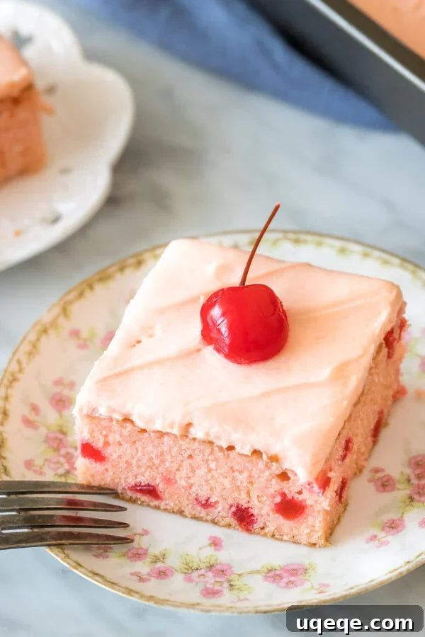Slice of cherry cake with cherry frosting and a cherry on top.