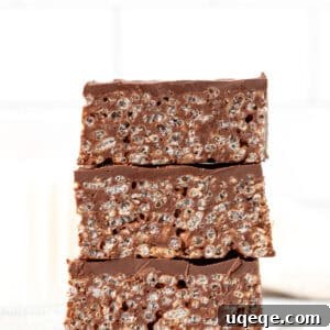 Three chocolate Rice Krispie treats, stacked one on top of another, showcasing the gooey texture and chocolate topping.