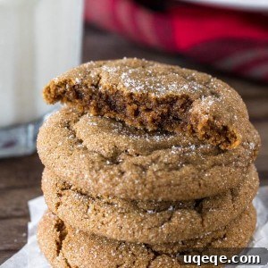 A stack of thick ginger molasses cookies with the top cookie broken in half, showcasing its soft interior.