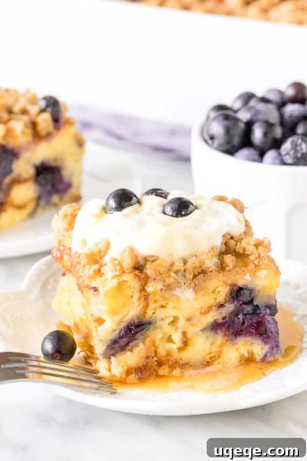 Overnight Blueberry French Toast Bake 2 Slice of blueberry French toast casserole with whipped cream on top and drizzled in syrup. Bowl of blueberries and second piece in the background.