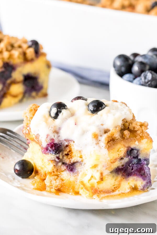 Overnight Blueberry French Toast Bake 4 Slice of french toast bake with bite taken out of it. Whipped cream on top melting down the sides.