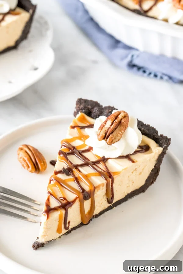 Decadent Slice of No-Bake Turtle Pie A perfectly sliced piece of no-bake turtle pie resting on a white plate, elegantly drizzled with golden caramel and rich chocolate sauce. The distinct layers of the crunchy Oreo crust, creamy caramel filling, and a scattering of toasted pecans are clearly visible, promising a delightful texture and flavor experience.