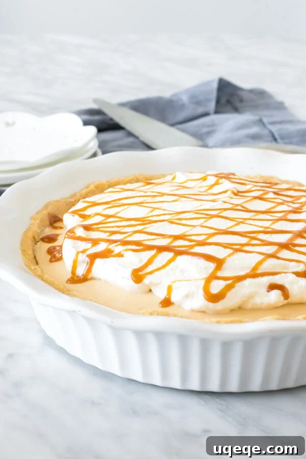 Golden Caramel Bliss Pie 3 A full no-bake salted caramel cream pie in a white pie plate, beautifully topped with generous swirls of whipped cream and a rich caramel sauce drizzle.