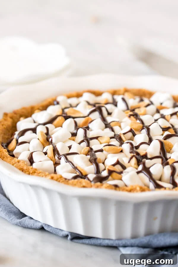 Decadent Rocky Road Pie 3 A full rocky road cheesecake pie in a pie pan, generously topped with marshmallows, peanuts, and a swirl of chocolate, ready for chilling.