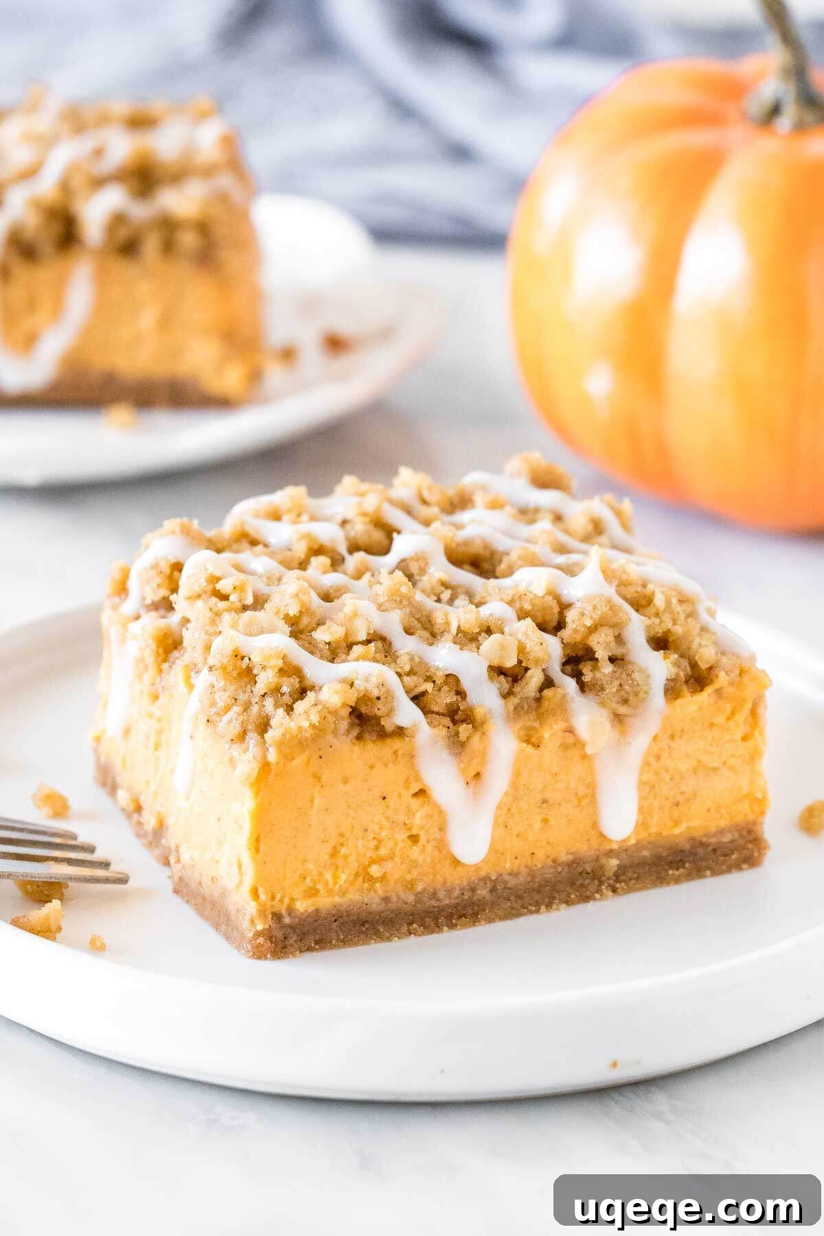 A delectable slice of pumpkin streusel bar artfully placed on a plate, with another tempting piece blurred in the background, showcasing its three luscious layers: crust, creamy filling, and golden streusel.