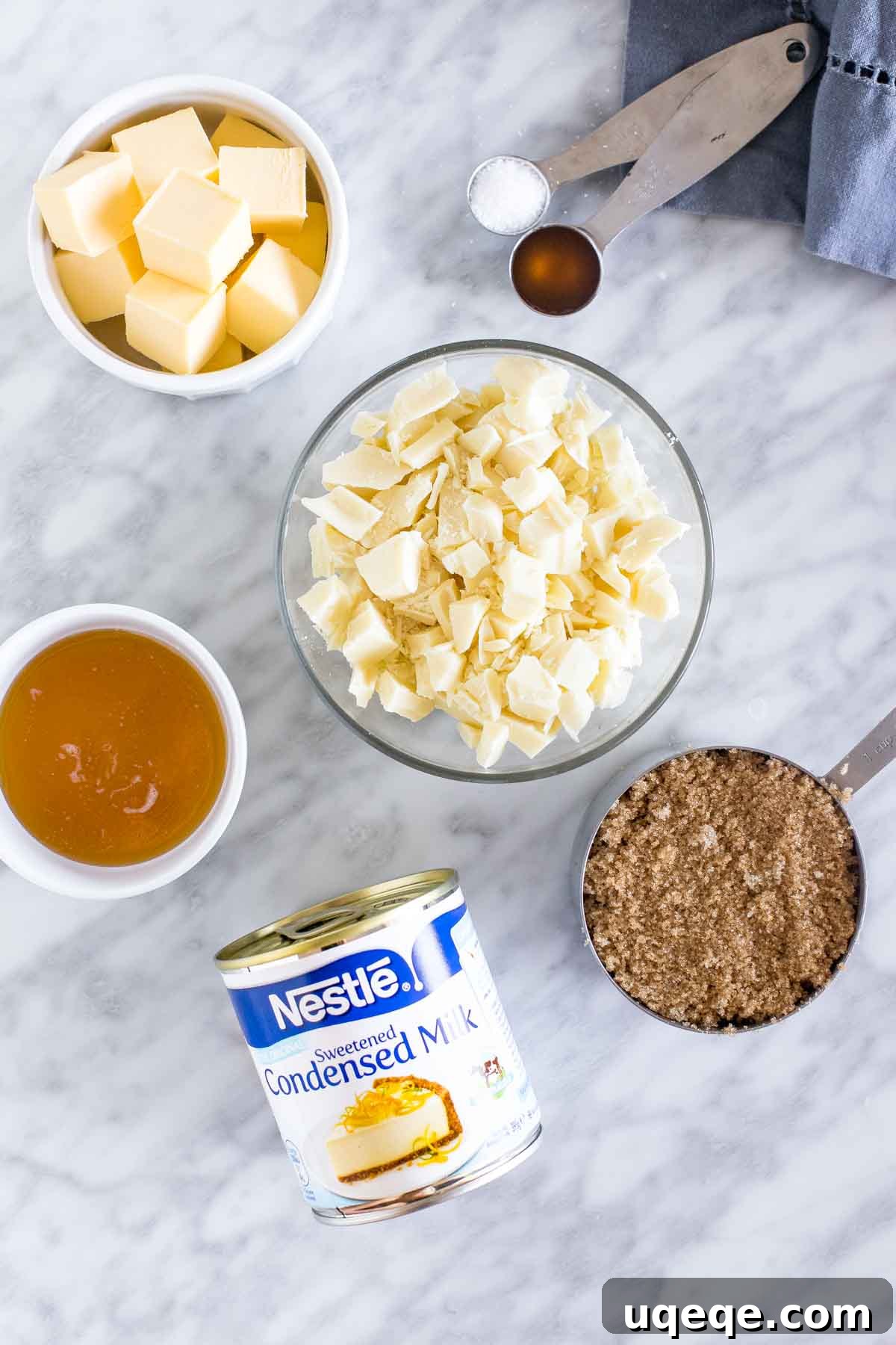 Effortless Condensed Milk Caramel Fudge 3 Ingredients for making creamy caramel fudge laid out on a wooden surface, including butter, brown sugar, sweetened condensed milk, and white chocolate