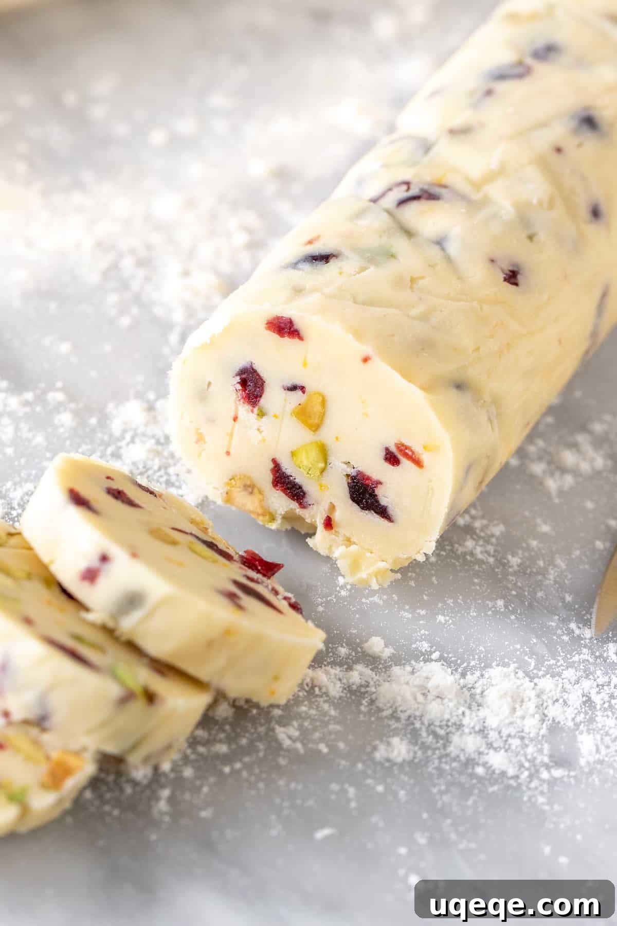 Jeweled Cranberry Pistachio Shortbread 4 An unbaked log of Cranberry Pistachio Shortbread cookie dough, partially sliced into individual cookies on a cutting board, ready for baking.
