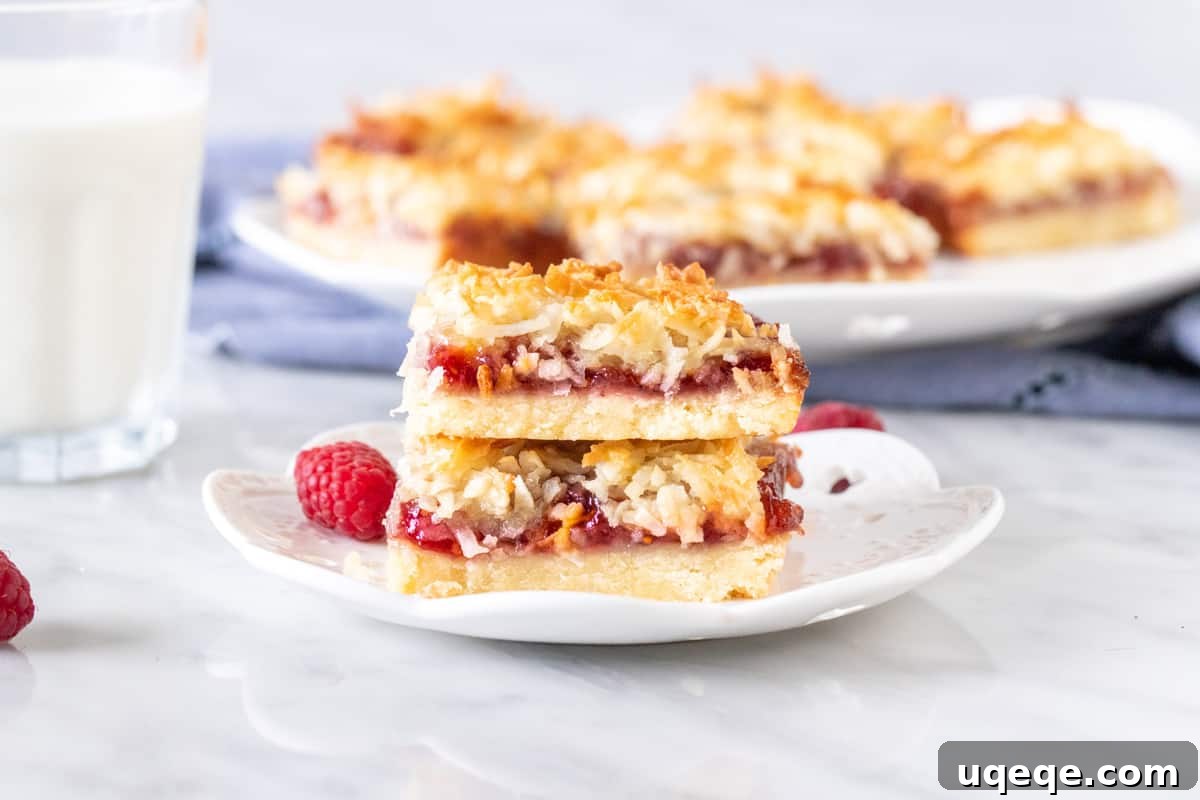 Raspberry Coconut Delights 6 Two raspberry jam bars with coconut topping, artfully stacked on a plate, highlighting their appealing layers and golden topping.