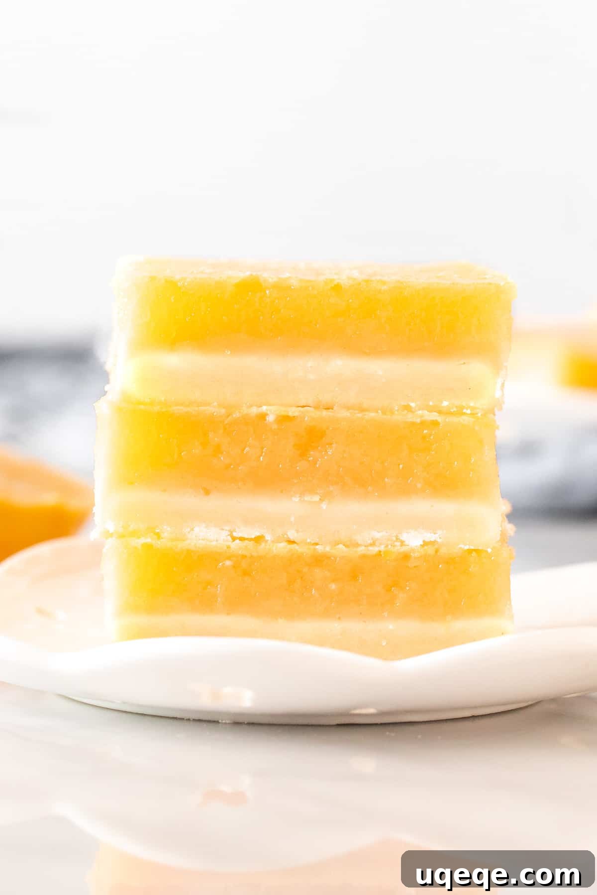 Stack of 3 golden lemon bars on a white plate, showcasing the buttery crust and bright yellow lemon layer, dusted with powdered sugar.