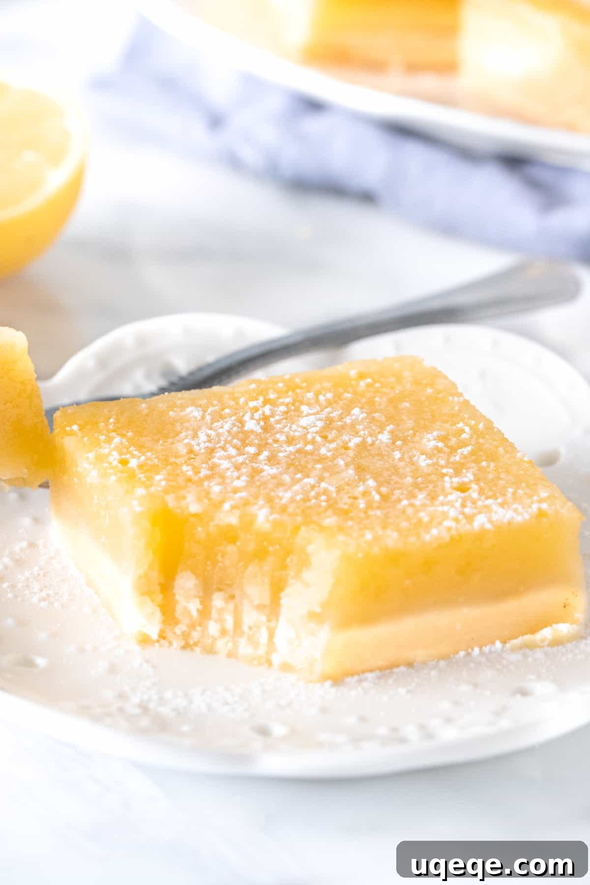 A single lemon bar with a bite taken out, resting next to a fresh lemon slice on a plate, highlighting its inviting texture.
