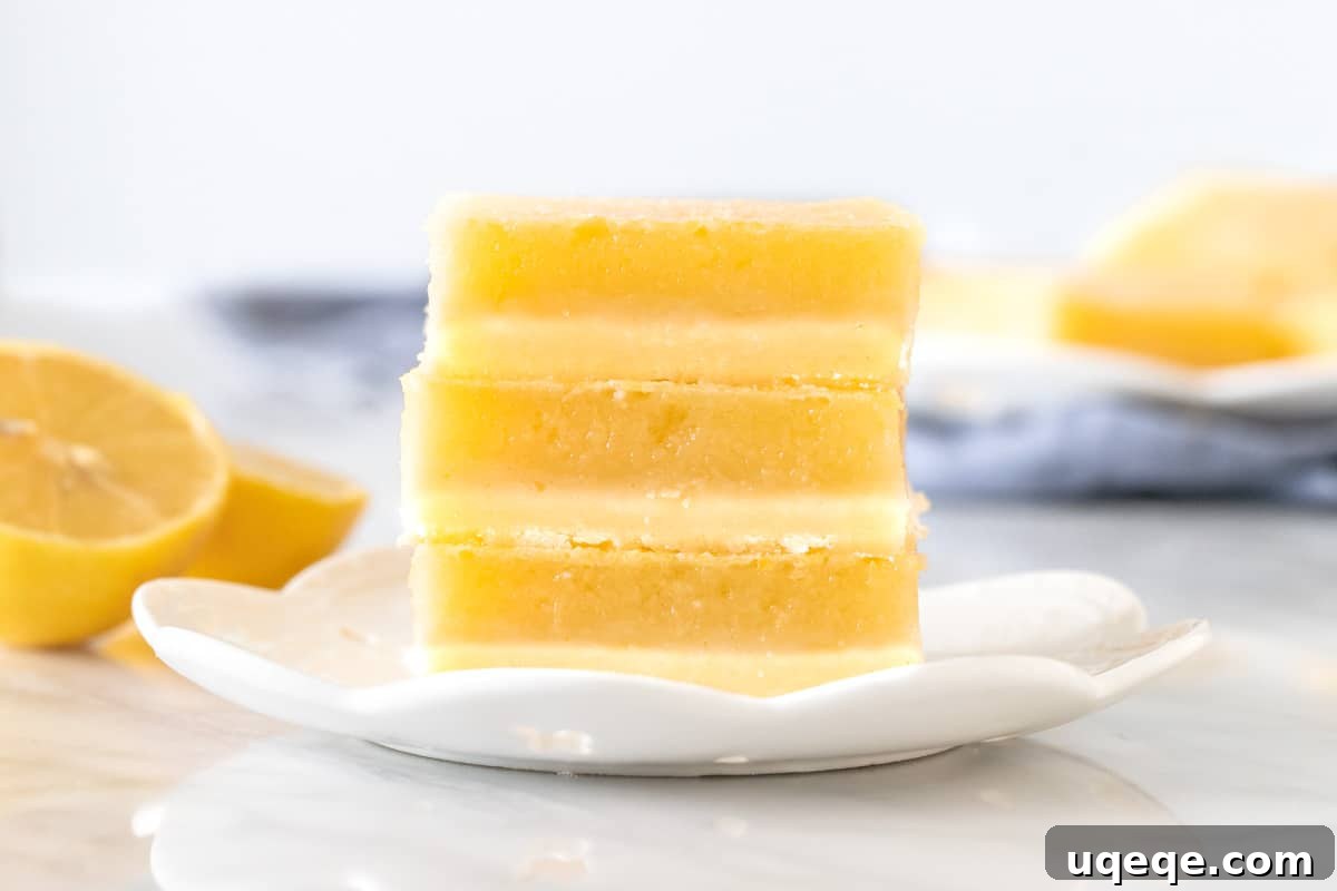Three perfectly stacked lemon bars on a white plate, showcasing the thick shortbread and glossy lemon topping.