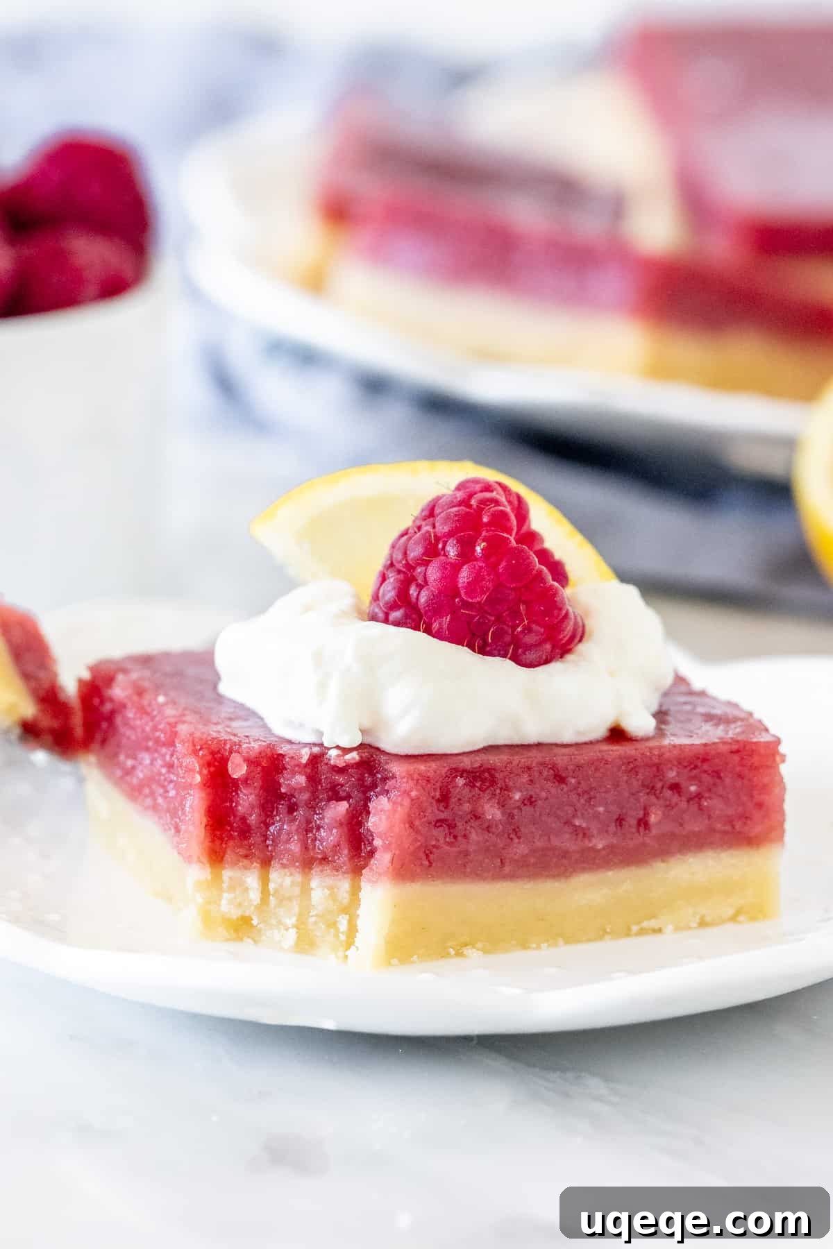 Sunshine Lemon Raspberry Bars 6 A single lemon raspberry bar on a white plate, topped with whipped cream and a fresh raspberry.