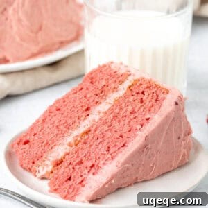 A perfect slice of homemade strawberry cake with creamy strawberry frosting, served alongside a refreshing glass of milk.