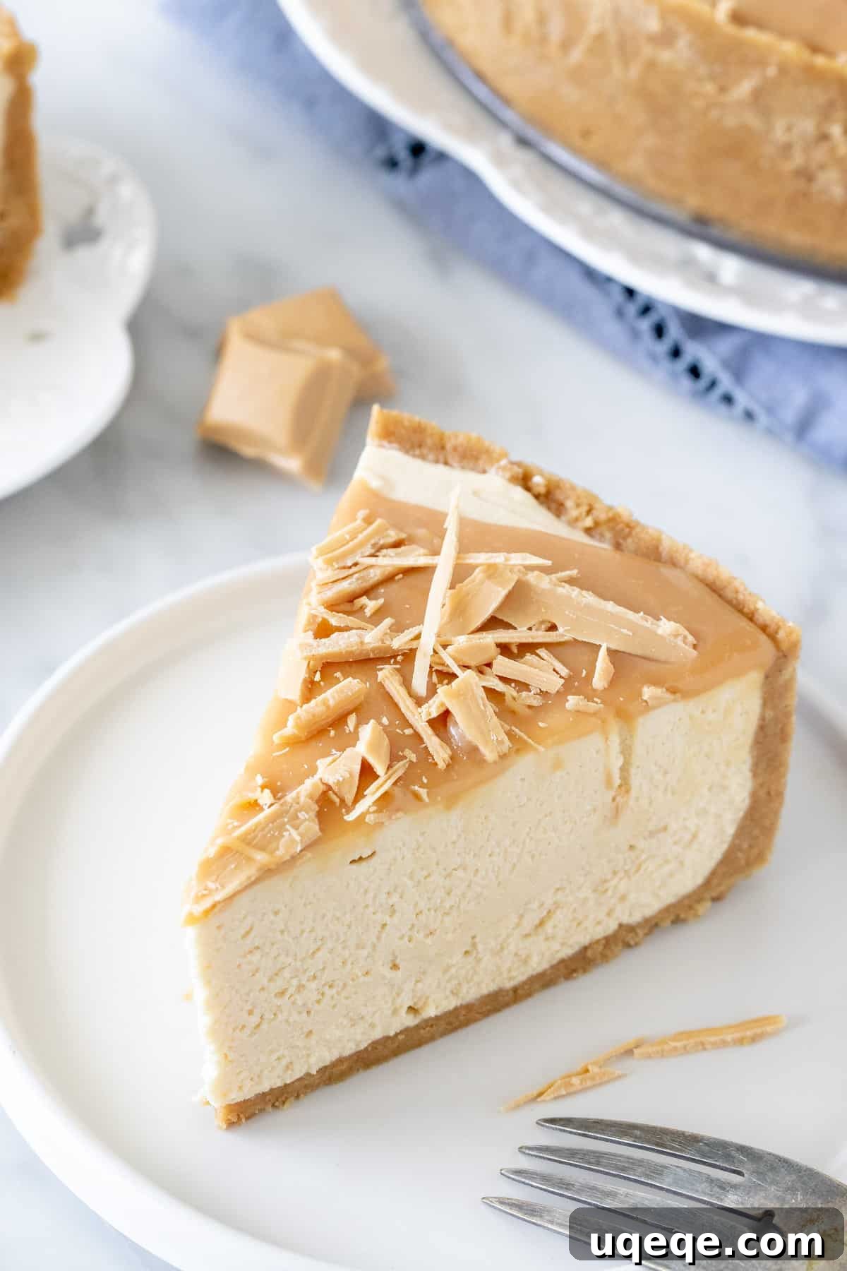 A perfectly sliced piece of Caramilk cheesecake served on a white plate, showcasing its creamy layers and golden caramelised white chocolate topping.