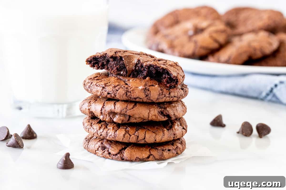Gourmet Brownie Cookies 8 A close-up of a stack of chocolate cookies, with the top cookie broken in half, revealing its moist, gooey, and irresistible fudgy interior.