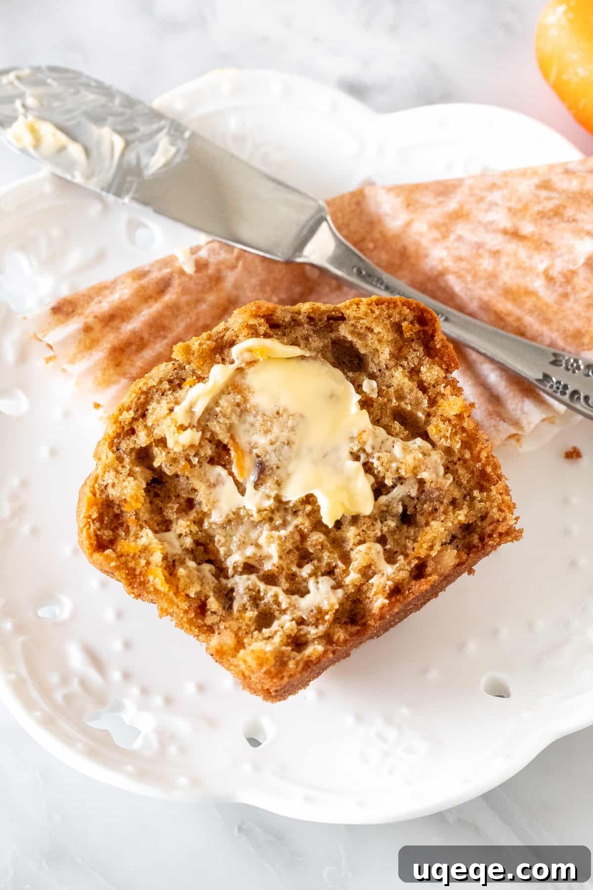 A perfectly baked carrot cake muffin, cut in half to reveal its moist, spiced interior, with a dollop of butter.