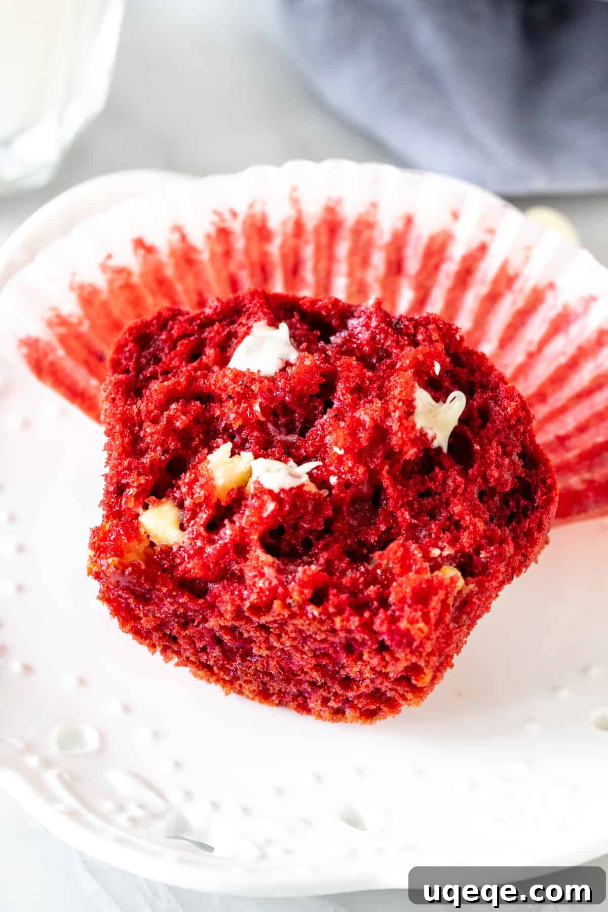A perfectly baked red velvet muffin, split in half to reveal its moist interior and melted chocolate chips, resting on a plate.