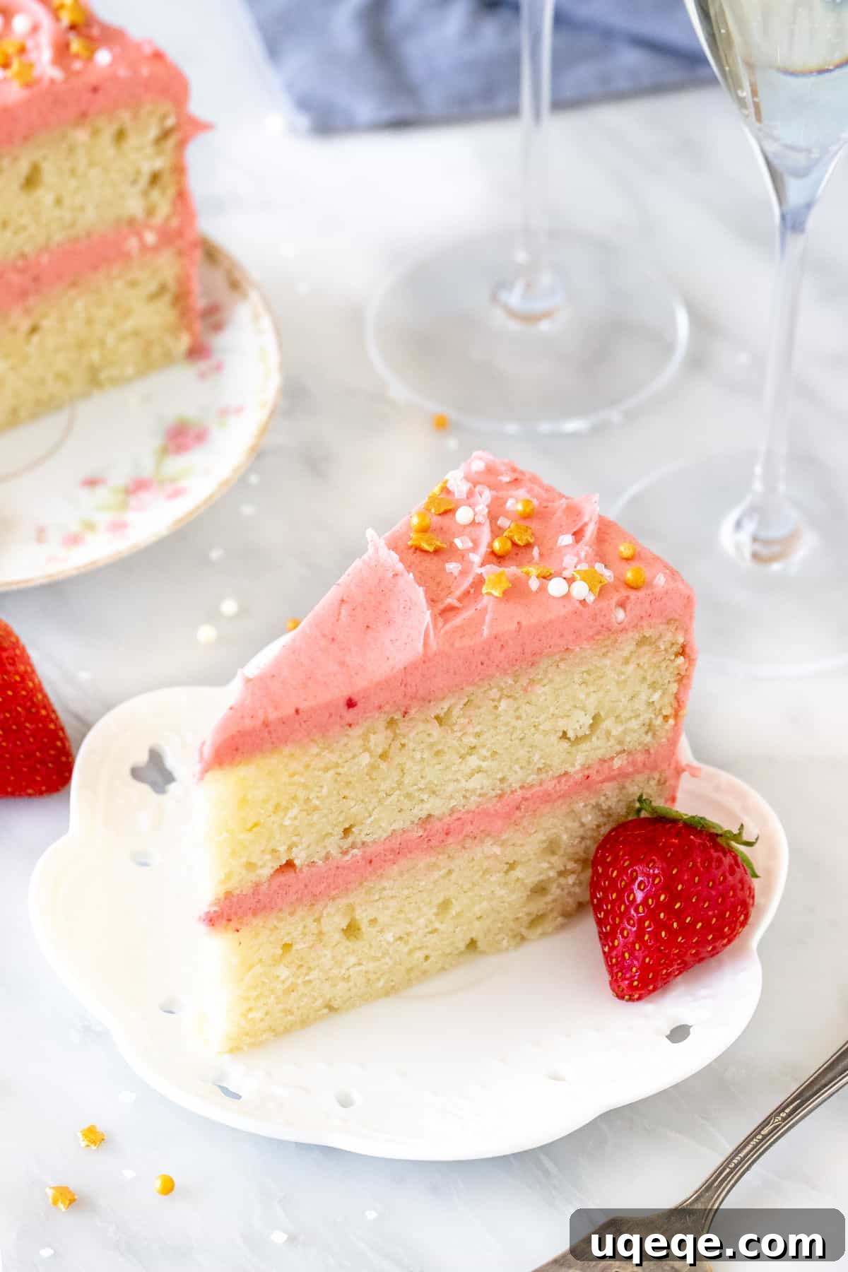 Sparkling Strawberry Bliss Cake 4 Slice of cake with vibrant pink strawberry frosting and two glasses of sparkling wine