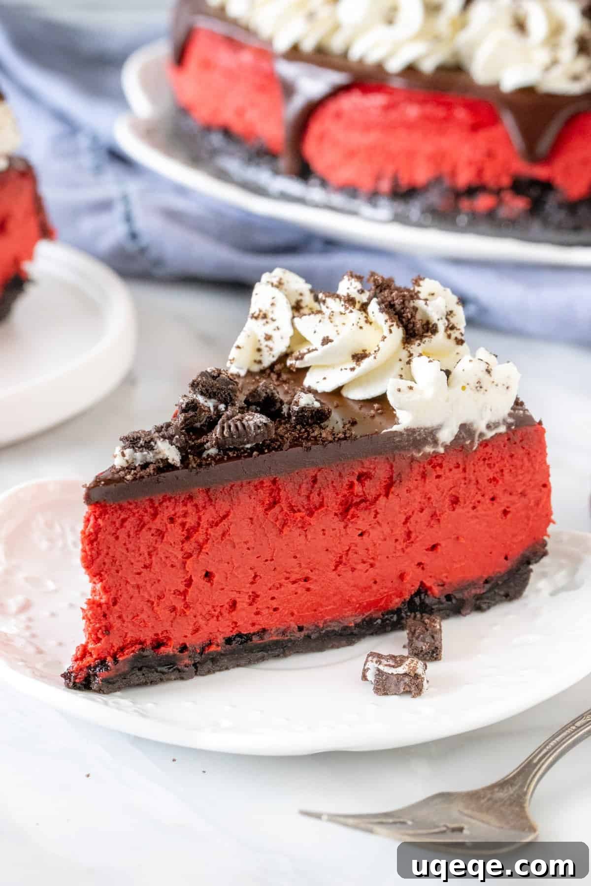 Velvety Oreo Dream Cheesecake 2 A beautifully presented slice of Red Velvet Oreo Cheesecake, showcasing its vibrant red filling, thick Oreo crust, and generous toppings of chocolate ganache, whipped cream, and crushed Oreos.