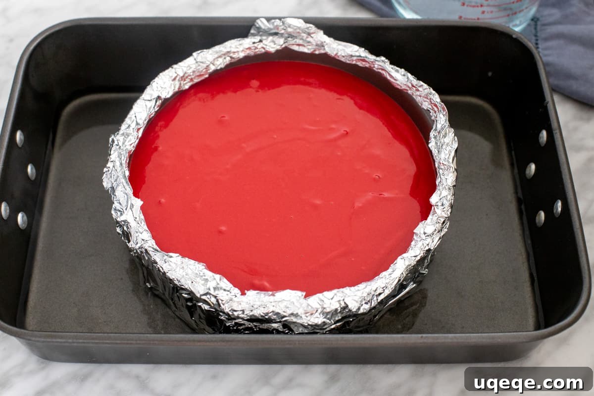 Velvety Oreo Dream Cheesecake 4 An unbaked Red Velvet Oreo Cheesecake filling resting in a foil-wrapped springform pan, placed inside a larger roasting pan for a water bath, ready to be baked in the oven.