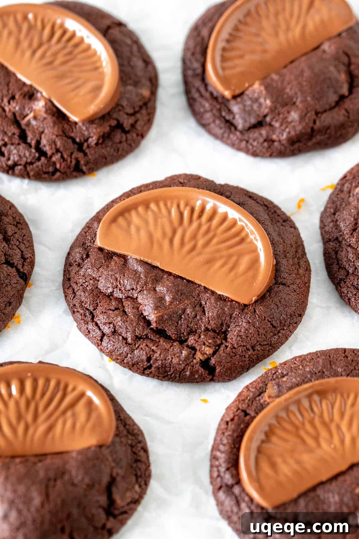 Zesty Chocolate Orange Delights 2 Fudgy chocolate orange cookies with melted chocolate chunks on parchment paper.