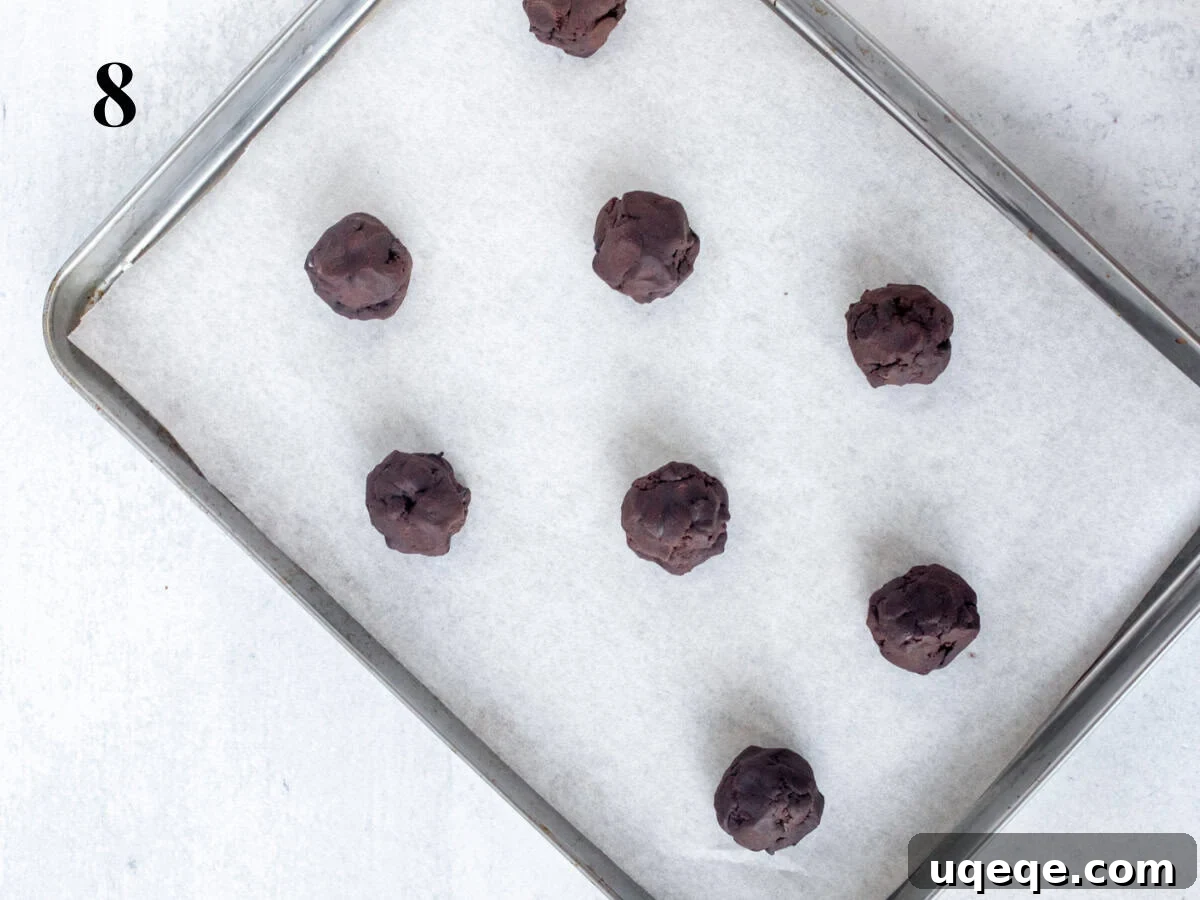 Decadent Double Chocolate Cookies 6 A baking sheet lined with parchment paper, topped with evenly spaced balls of double chocolate chip cookie dough, ready for the oven.