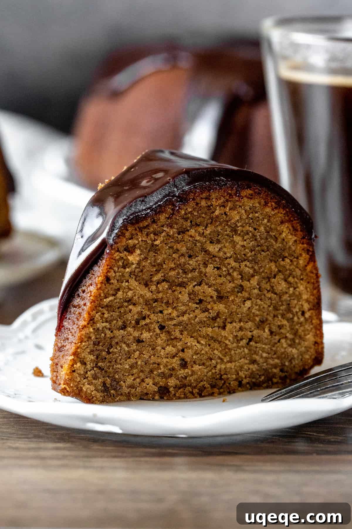 Velvet Coffee Bundt 2 A perfectly sliced coffee bundt cake revealing its moist interior, drizzled with chocolate ganache, resting on a white plate next to a cup of coffee