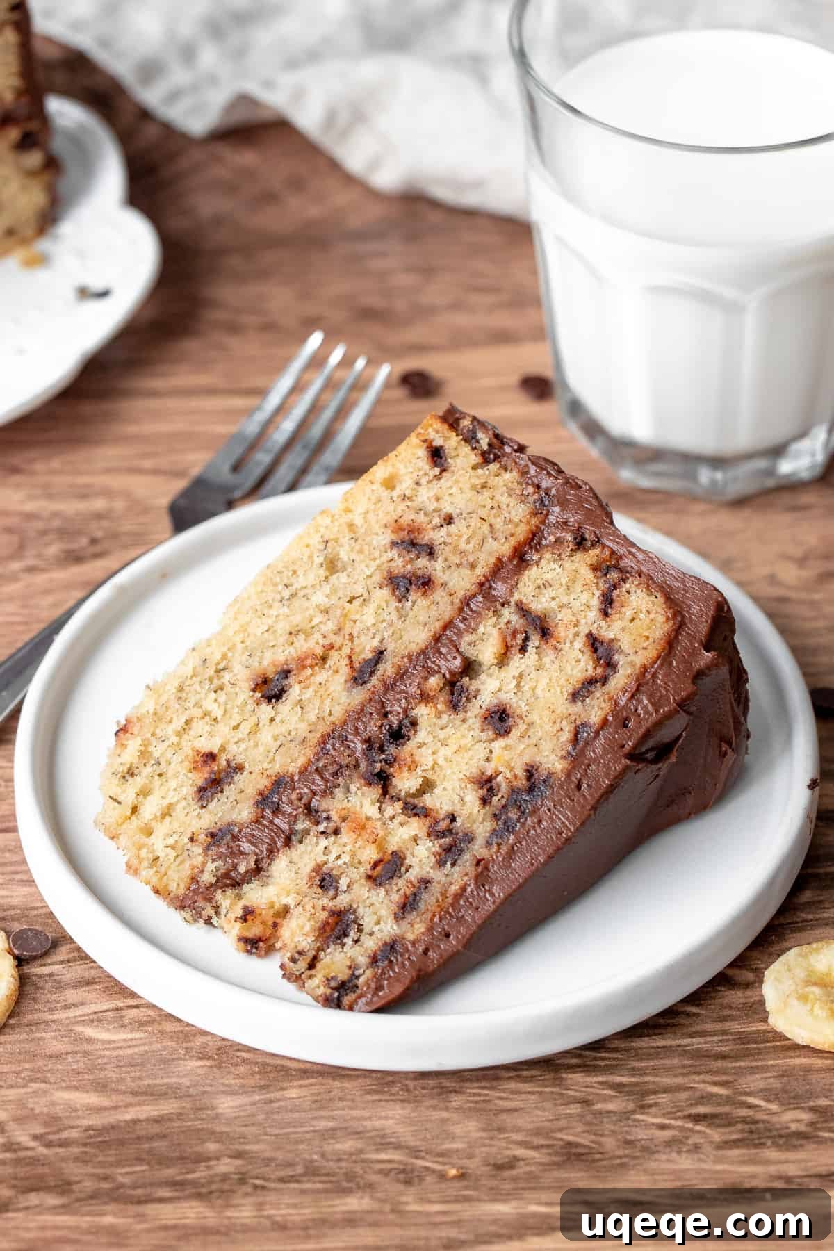 Decadent Banana Chocolate Chip Cake 2 Slice of banana chocolate chip cake with glass of milk, showcasing moist layers and chocolate chips with creamy frosting