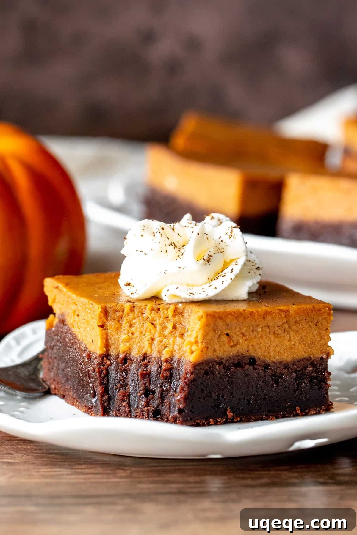 Layered Pumpkin Pie Fudgy Brownies 6 A slice of layered pumpkin pie brownie topped with a swirl of whipped cream on a white plate, ready to be enjoyed.