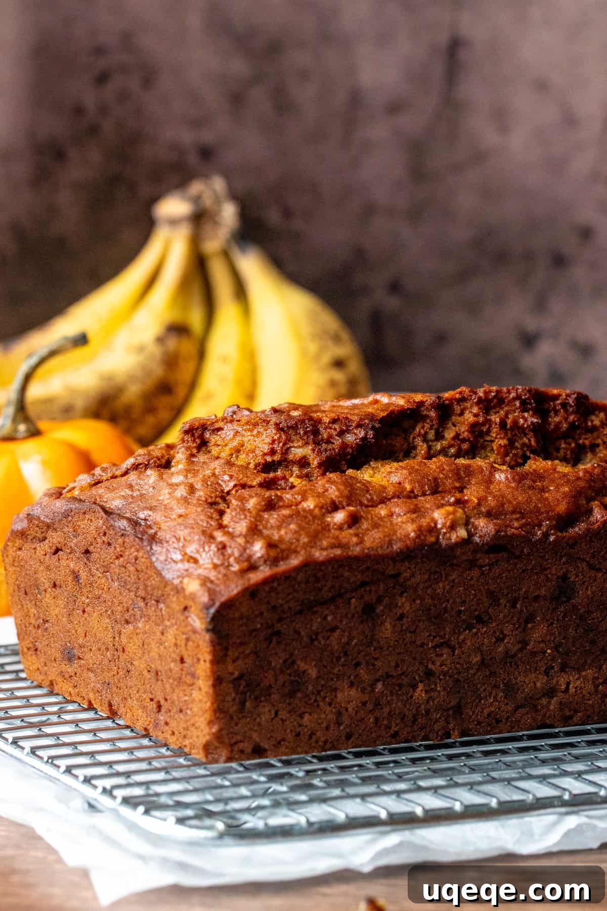 Loaf of pumpkin banana bread artfully arranged with brown bananas and a mini pumpkin, highlighting its autumn theme.