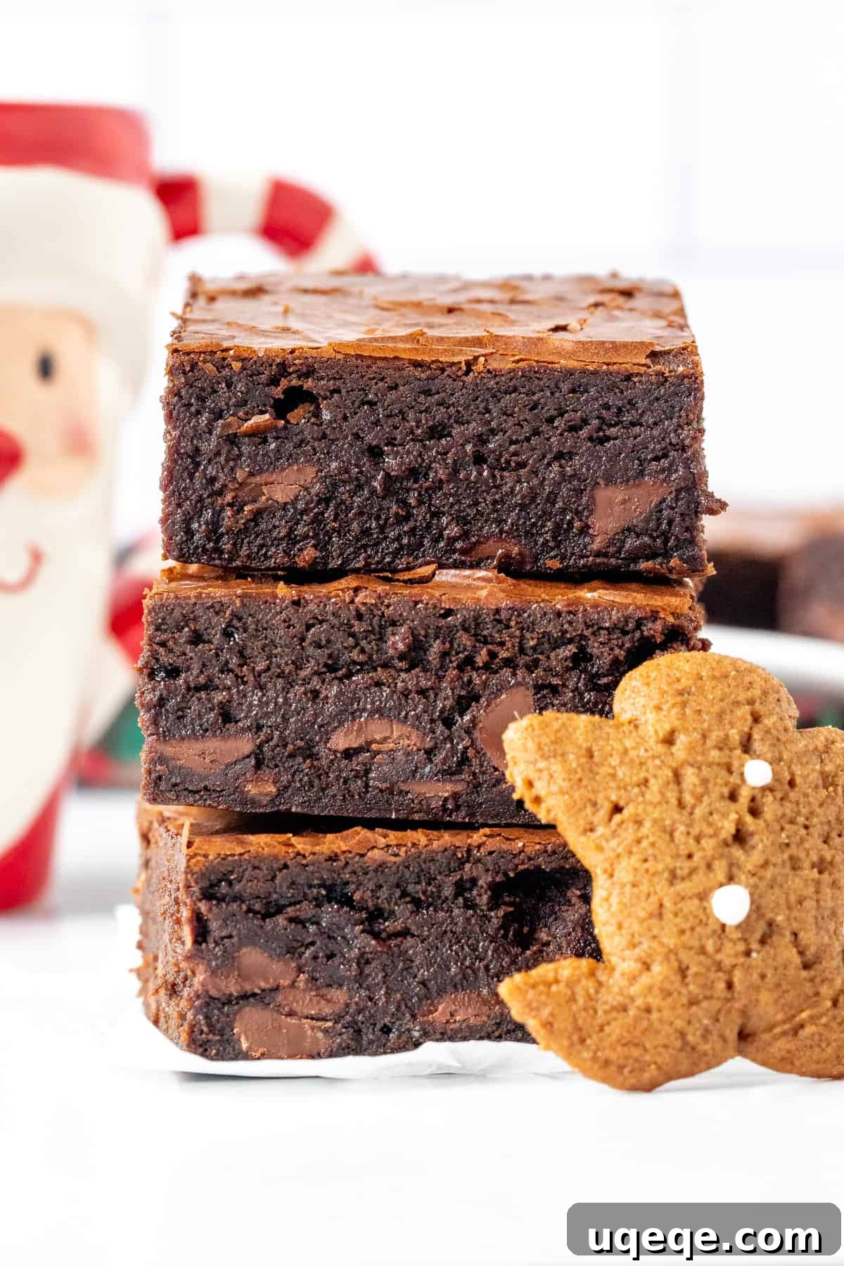 Stack of three thick, fudgy gingerbread brownies with a small gingerbread man cookie beside them, highlighting their crinkly tops and chocolate chips.